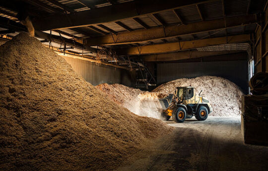 A loader moving a large pile of sawdust in a warehouse